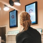 Photo of woman looking at advertising display in bathroom illustrates blog: "Print or Digital Advertising: Which One Should You Choose?"